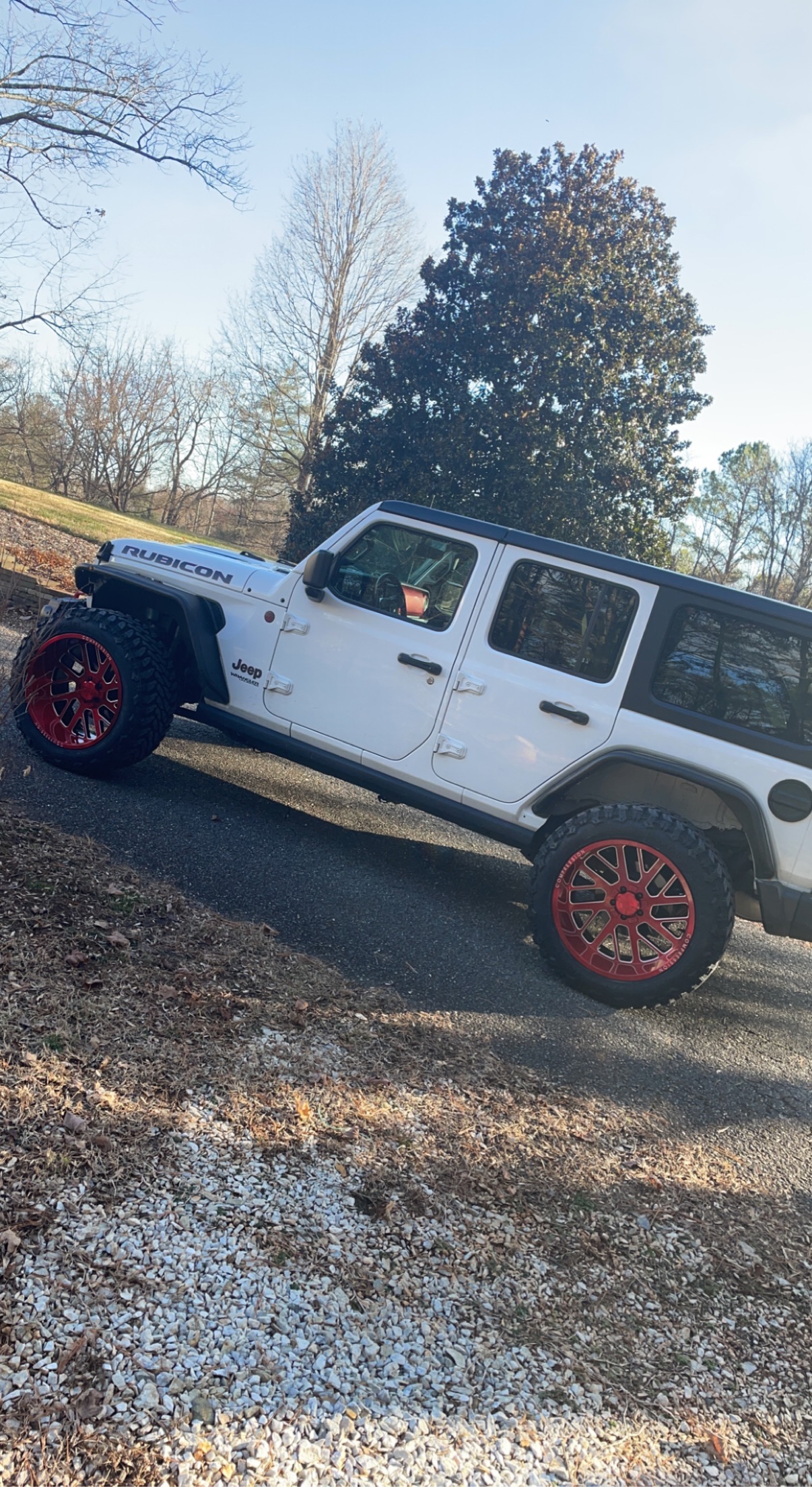 White Jeep Wrangler Rubicon with red wheels parked outdoors.