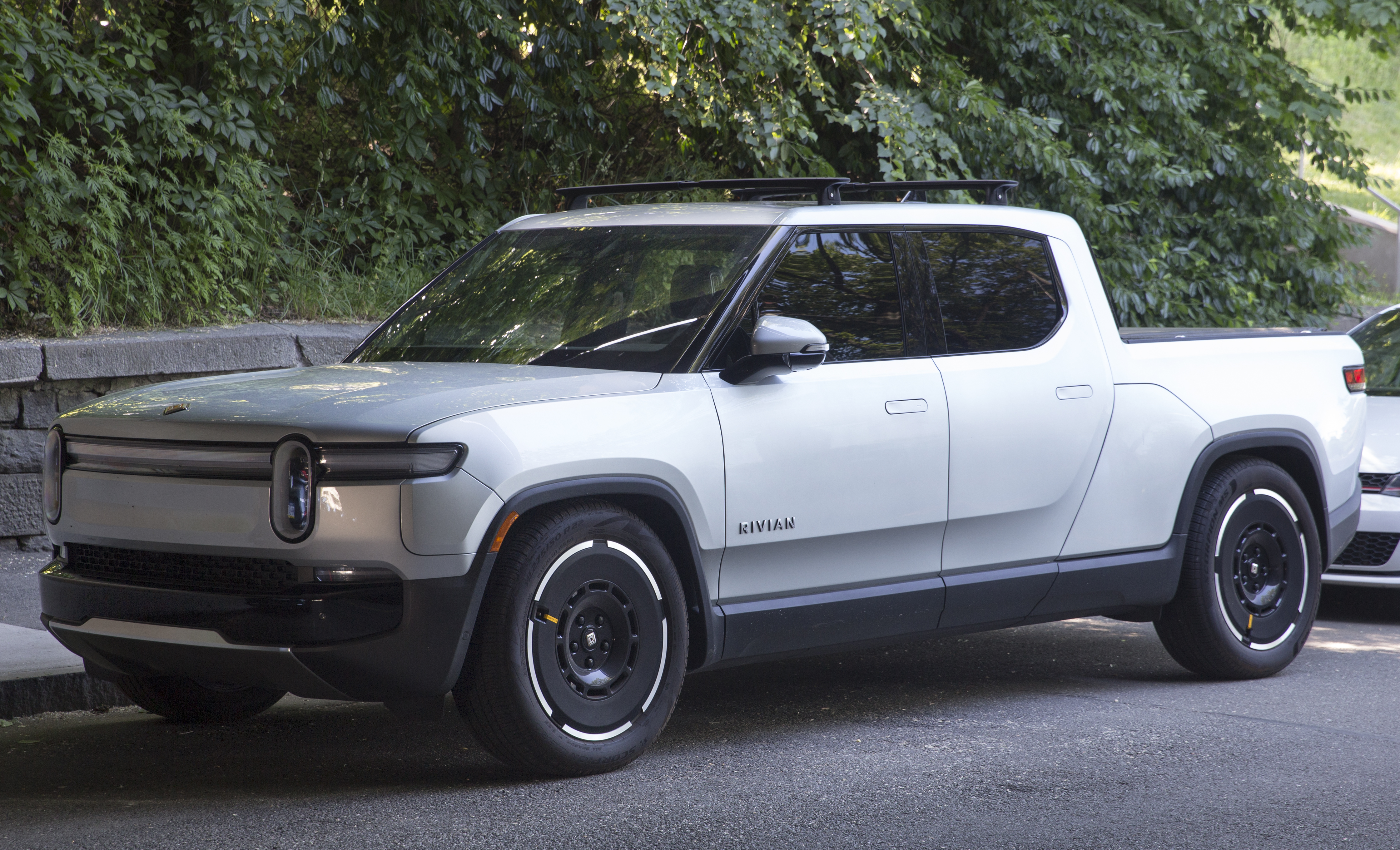 Silver Rivian R1T pickup parked beside trees.