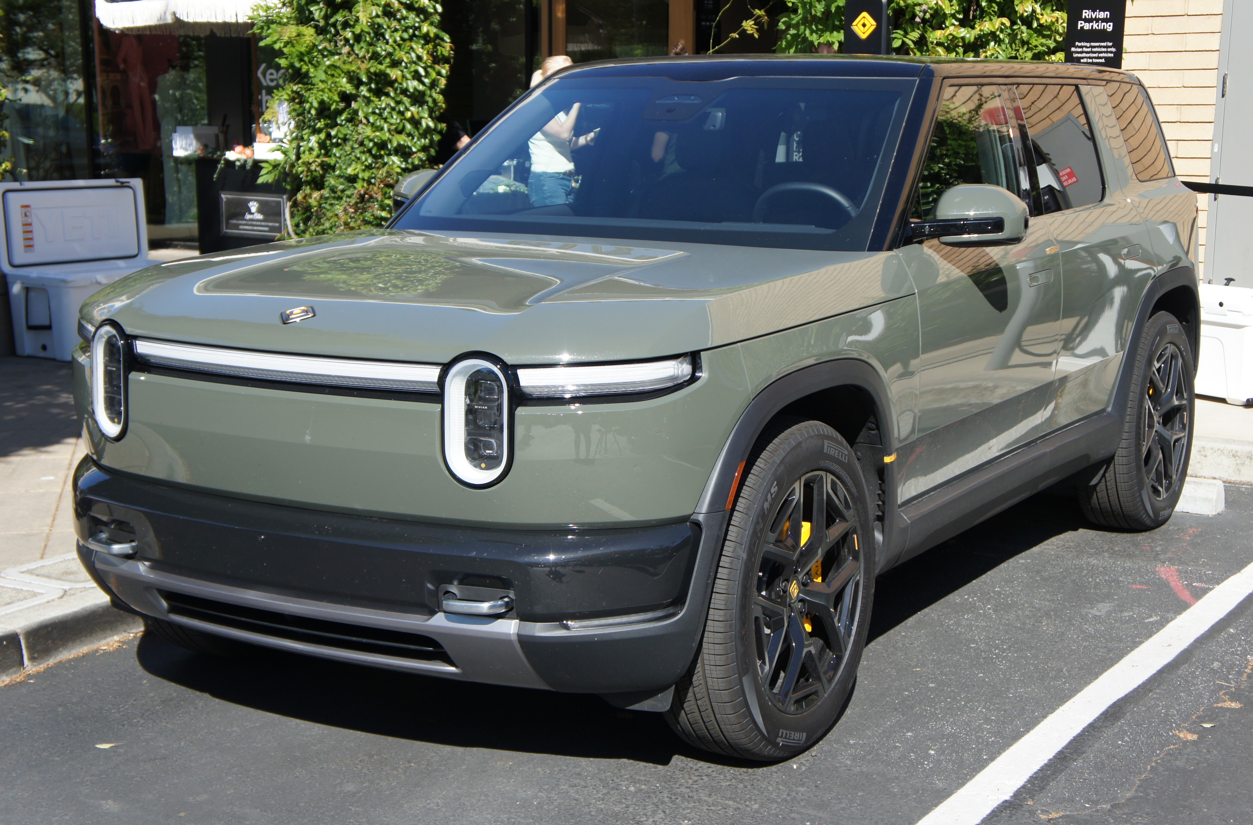 A green Rivian R2 parked outside a shopping center.