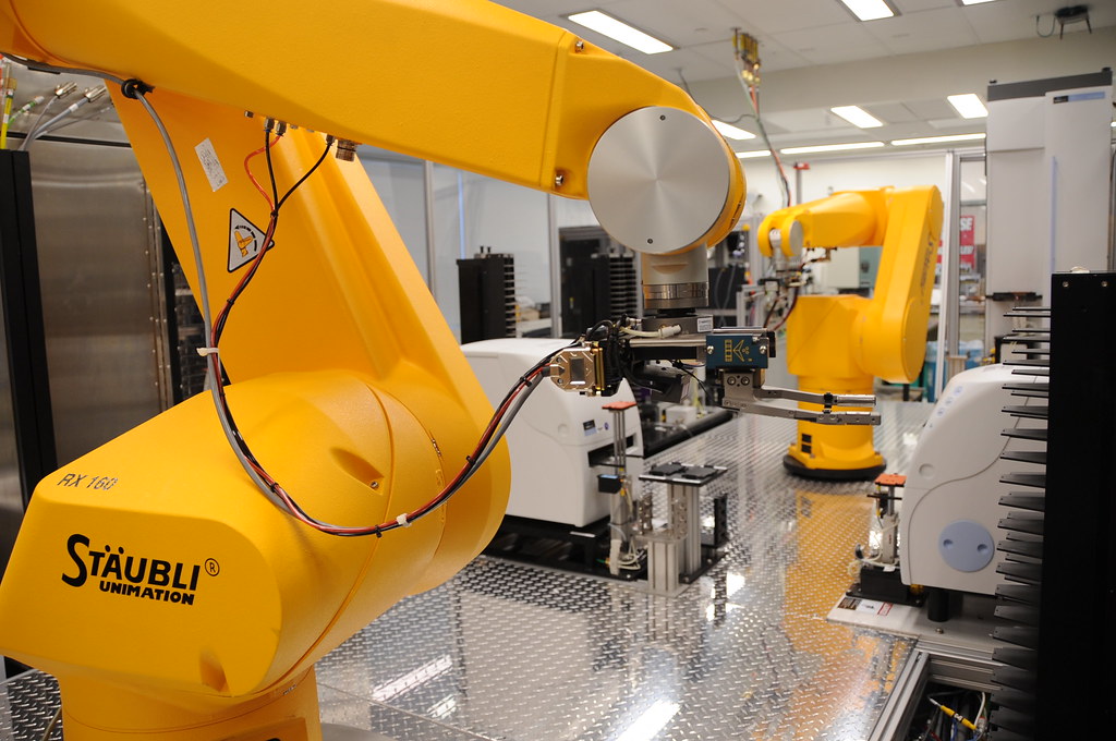 File photo: yellow robotic arms beside laboratory plate-handling equipment.