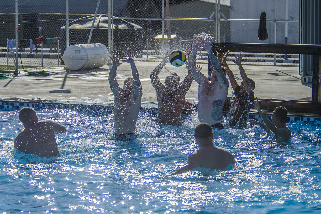 Service members play water polo in an outdoor pool.