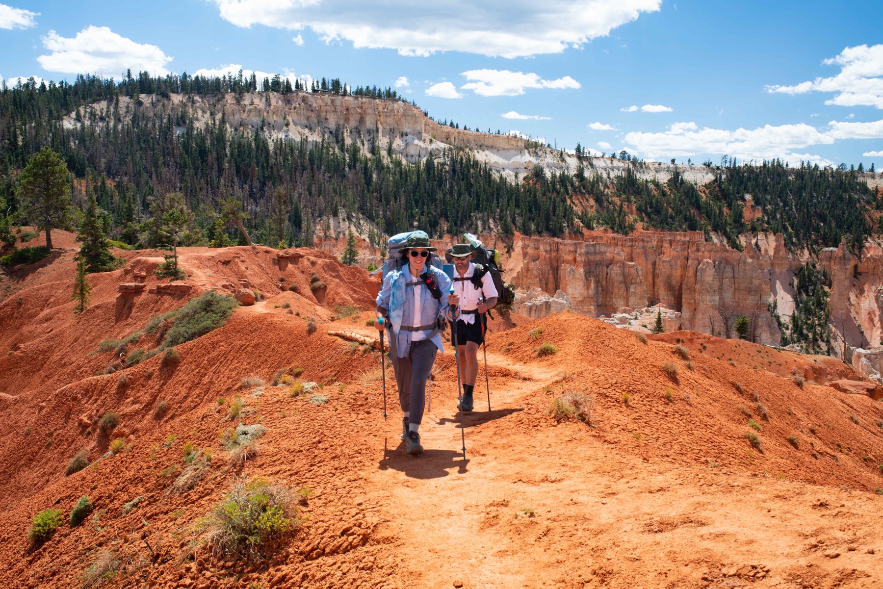 Two hikers follow a red-dirt trail beneath Bryce Canyon formations.