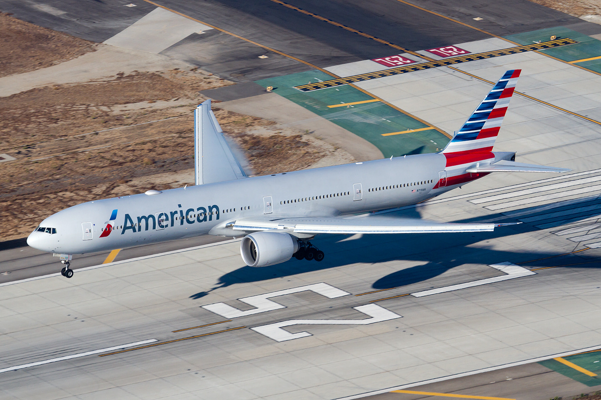 An American Airlines jet with landing gear extended above a runway.