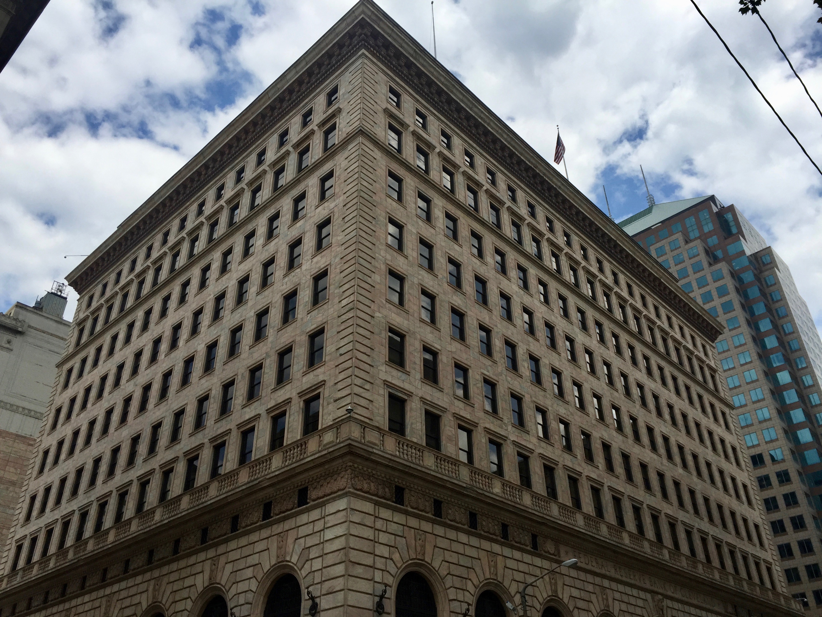 Stone corner of the Federal Reserve Bank of Cleveland, viewed from below beside a glass building.