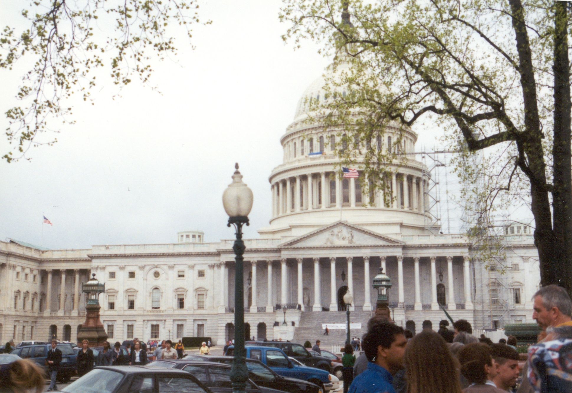 Archival view of the U.S. Capitol’s east front and dome, with trees and visitors in the foreground.