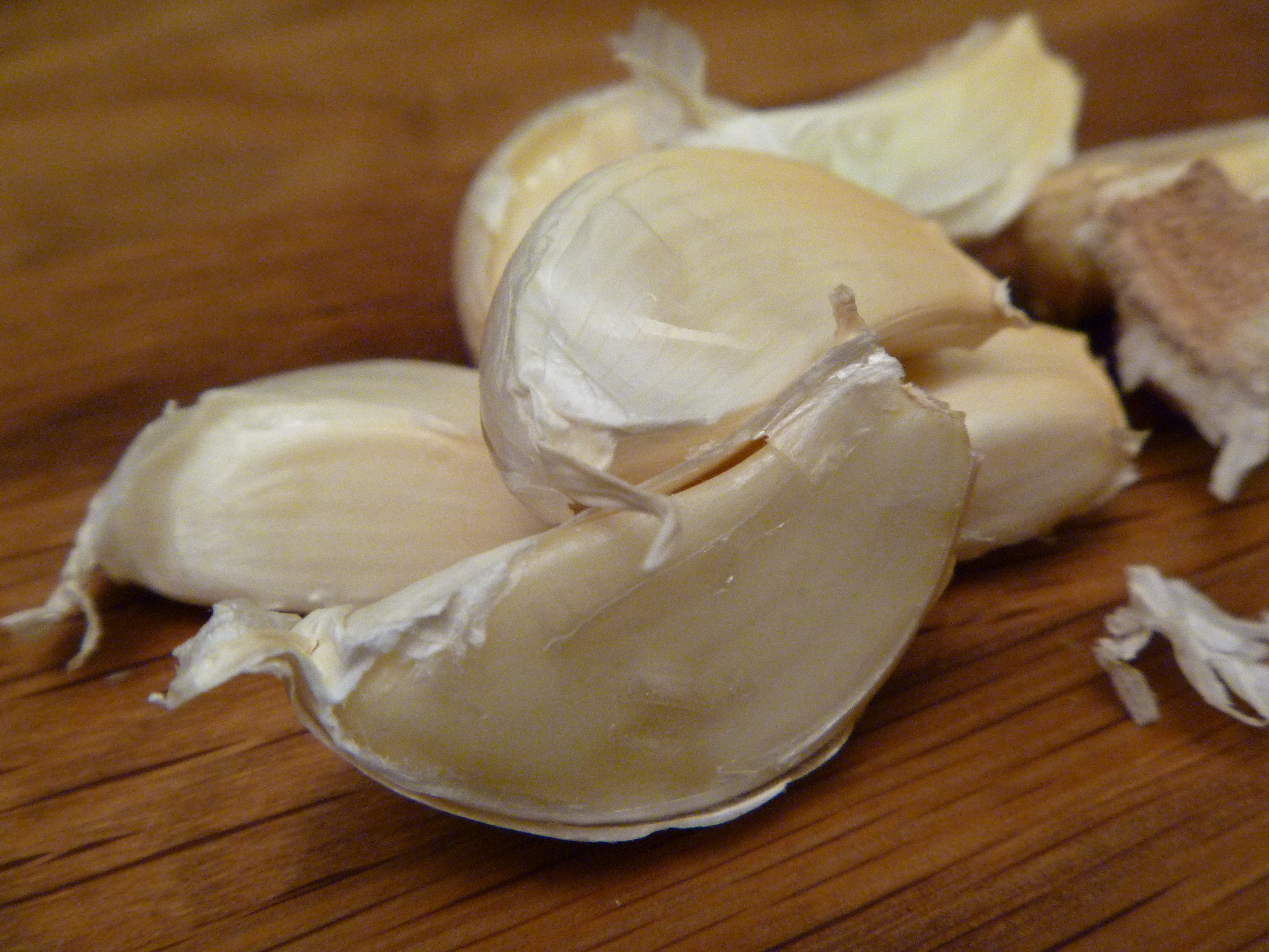 Garlic cloves rest on a wooden surface.