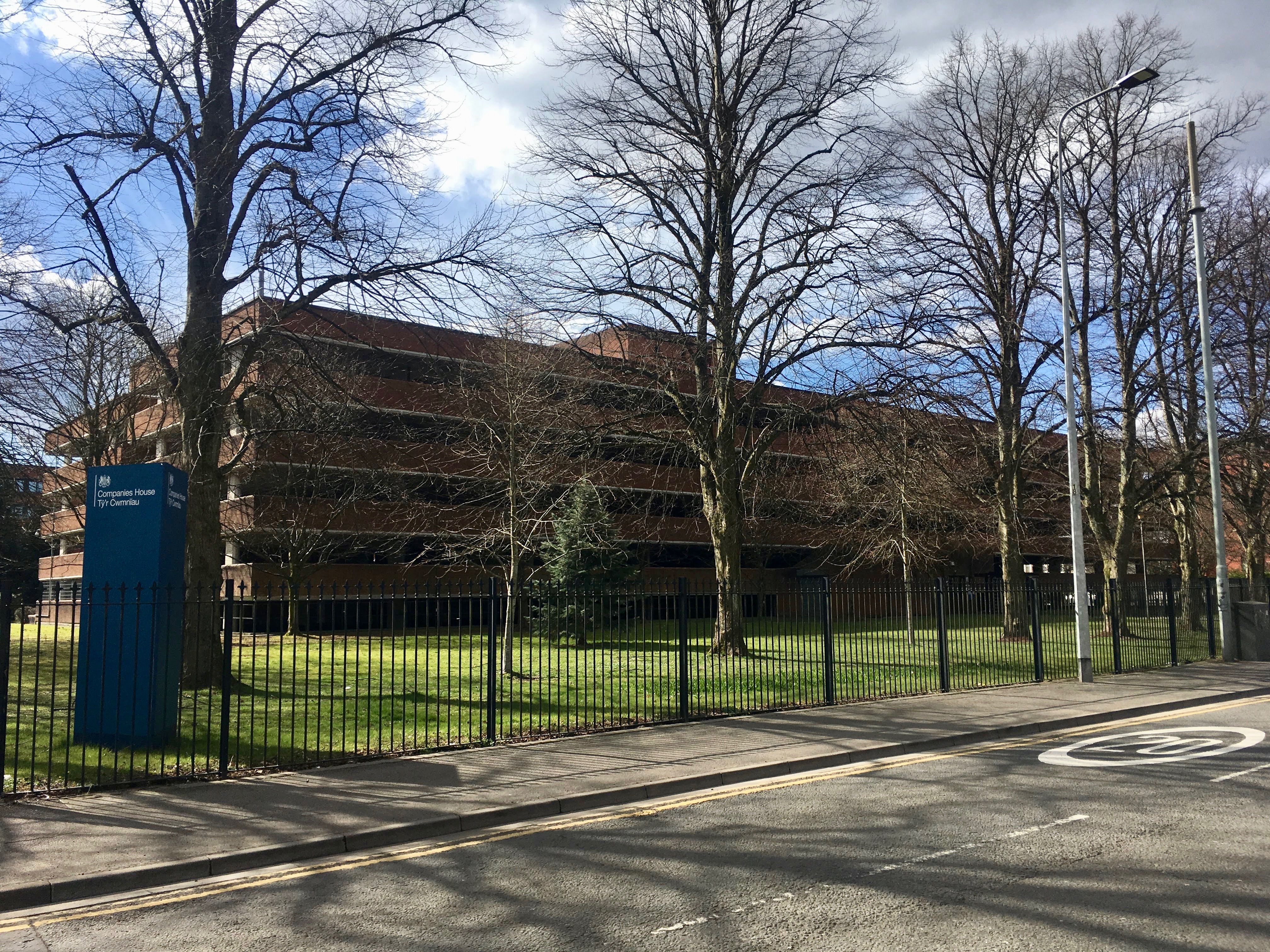 Companies House building, blue identification sign and roadside trees in Cardiff.