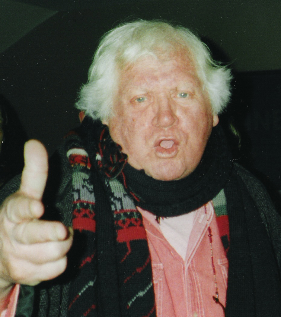 Ken Russell wearing a patterned scarf and raising his hand.