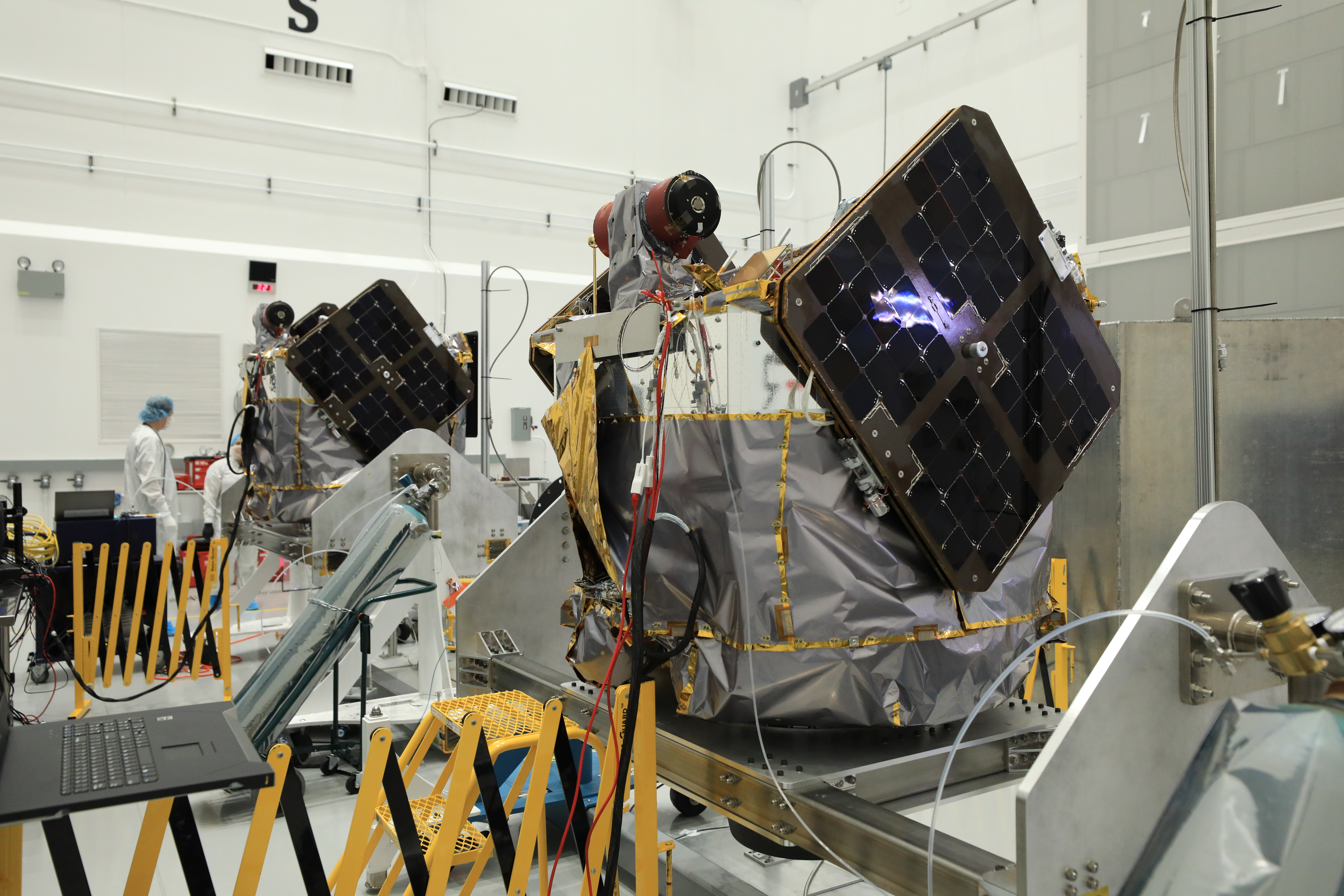 Two ESCAPADE spacecraft with dark solar panels stand on dollies inside a processing facility.
