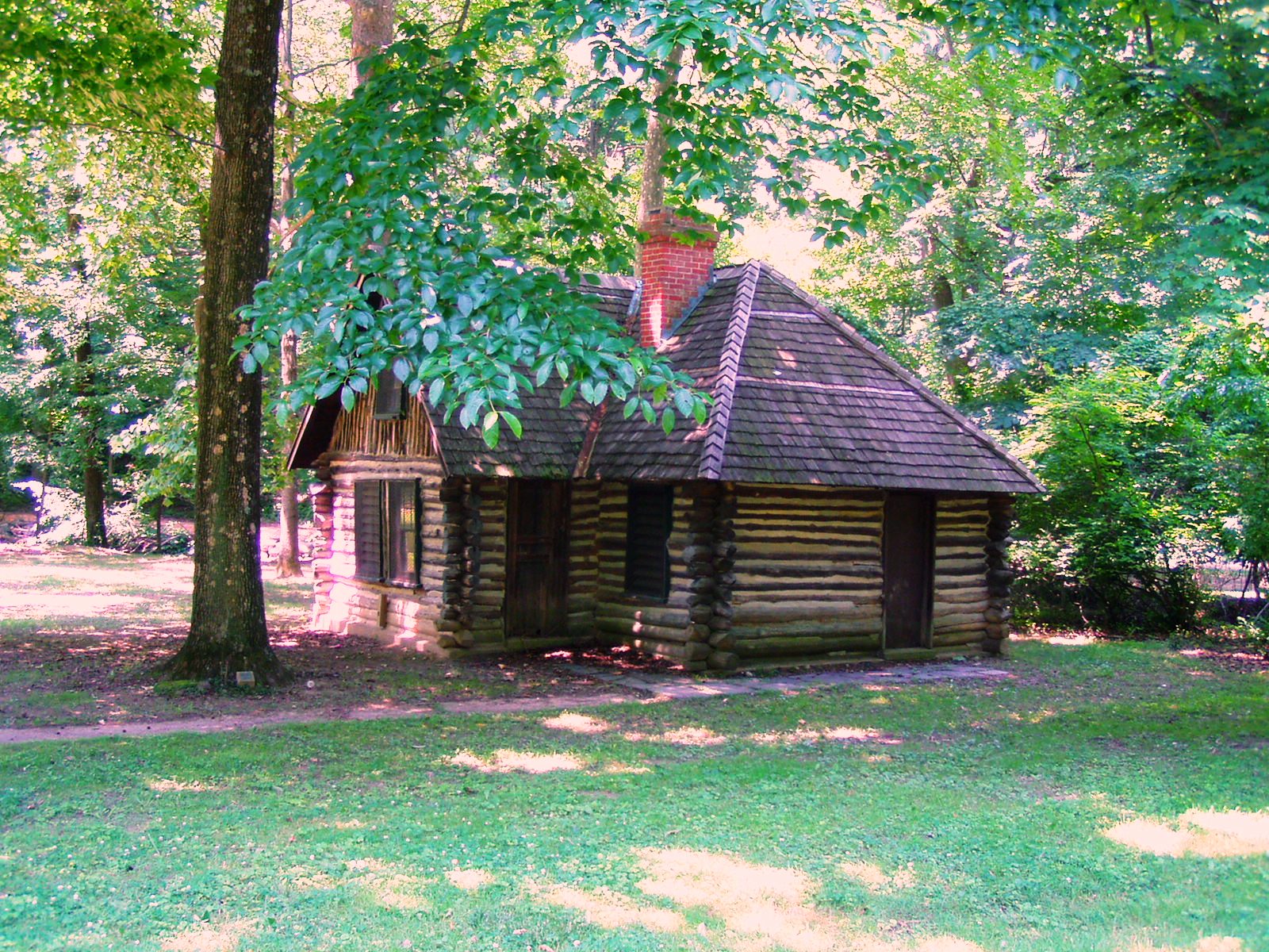 A log cabin with a brick chimney stands among trees.