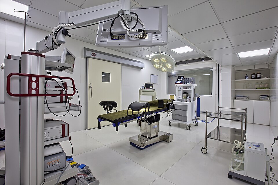 An empty operating theatre contains a surgical table and monitors.
