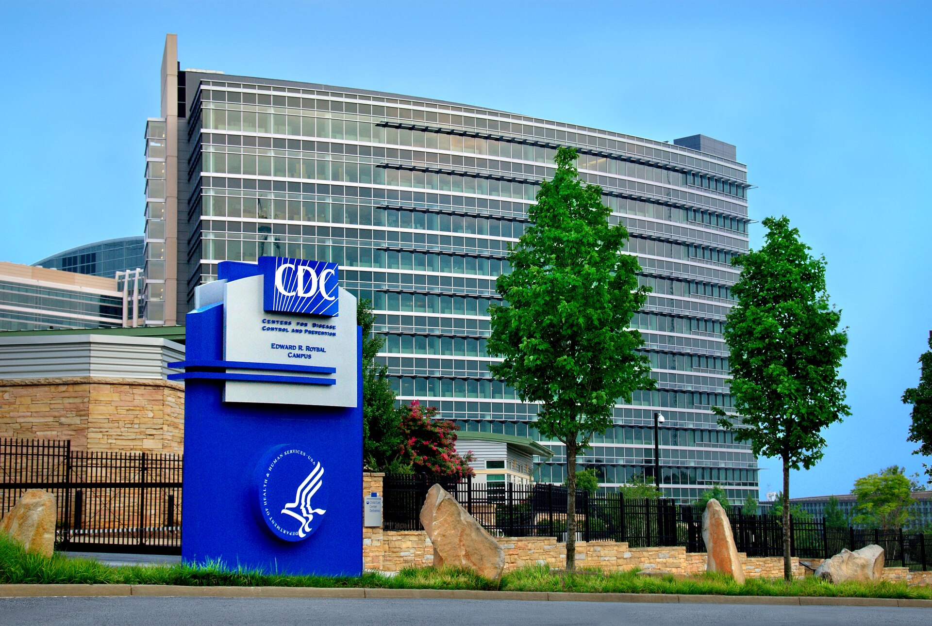 A CDC campus sign in front of a glass-fronted office building and trees.