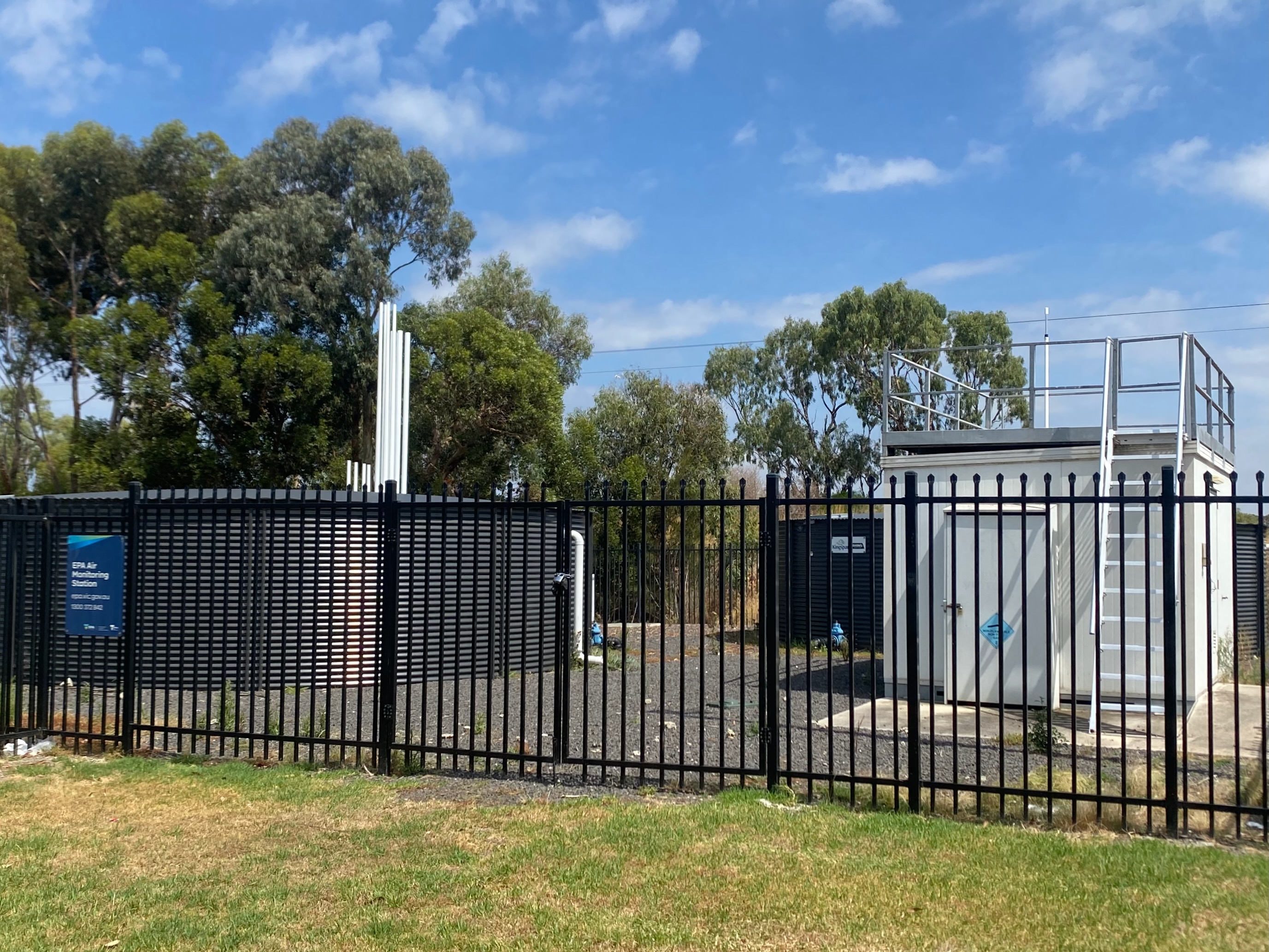 A fenced monitoring station with a rooftop platform, instrument inlets and an EPA sign.