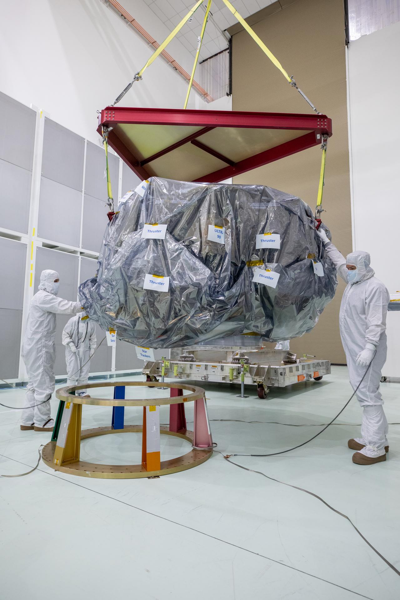 Technicians in cleanroom suits guide a wrapped IMAP spacecraft beneath a lifting frame.