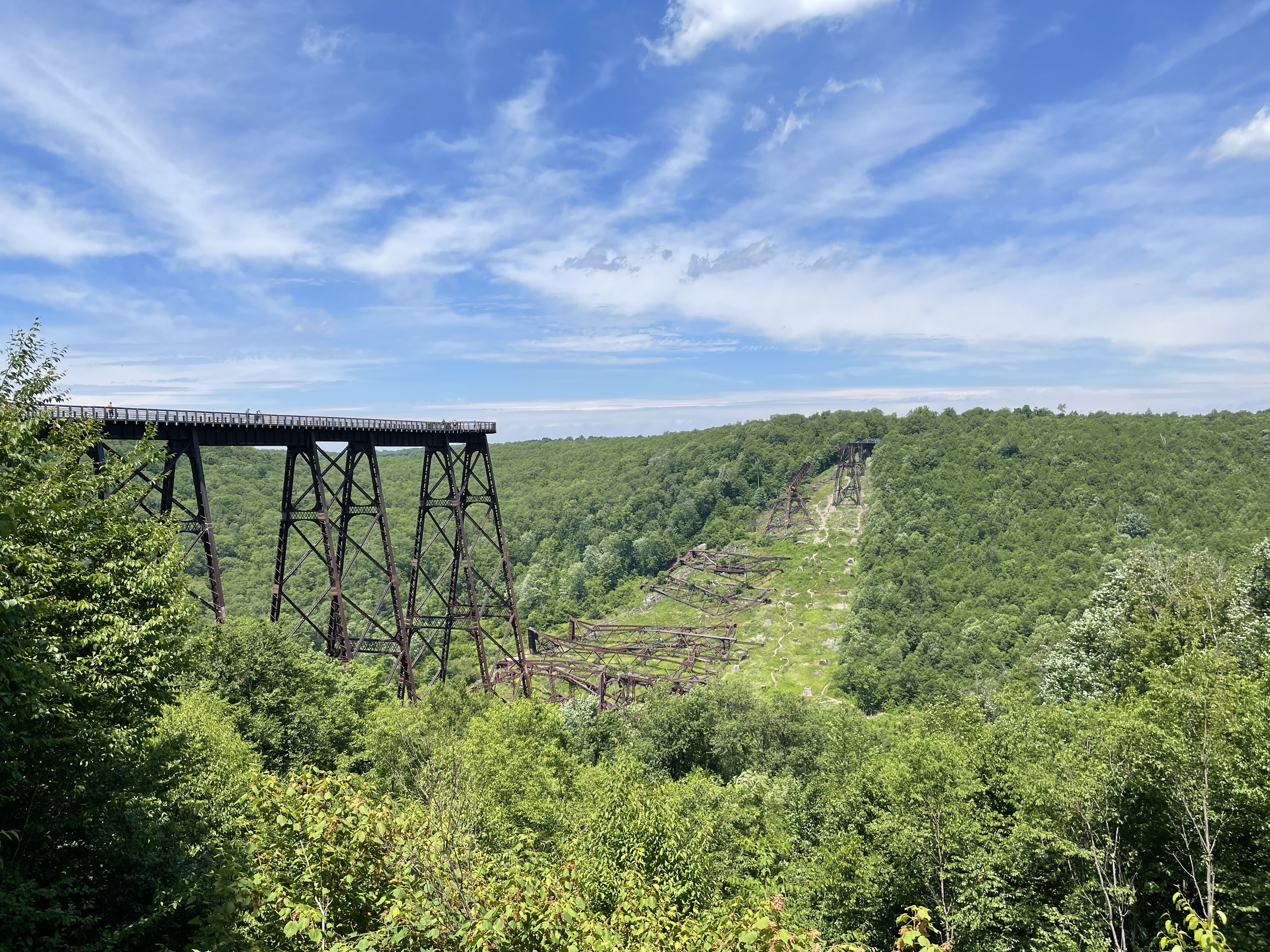 Surviving Kinzua Skywalk on steel towers at left, with collapsed bridge steelwork across a green wooded valley, photographed in July 2022.