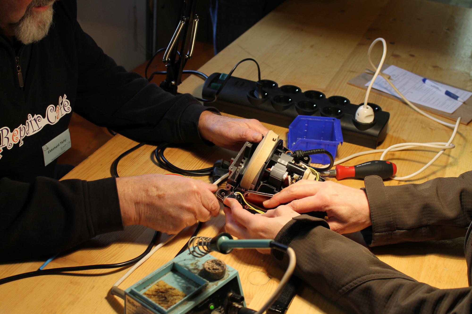 A volunteer works on an opened appliance at a table.
