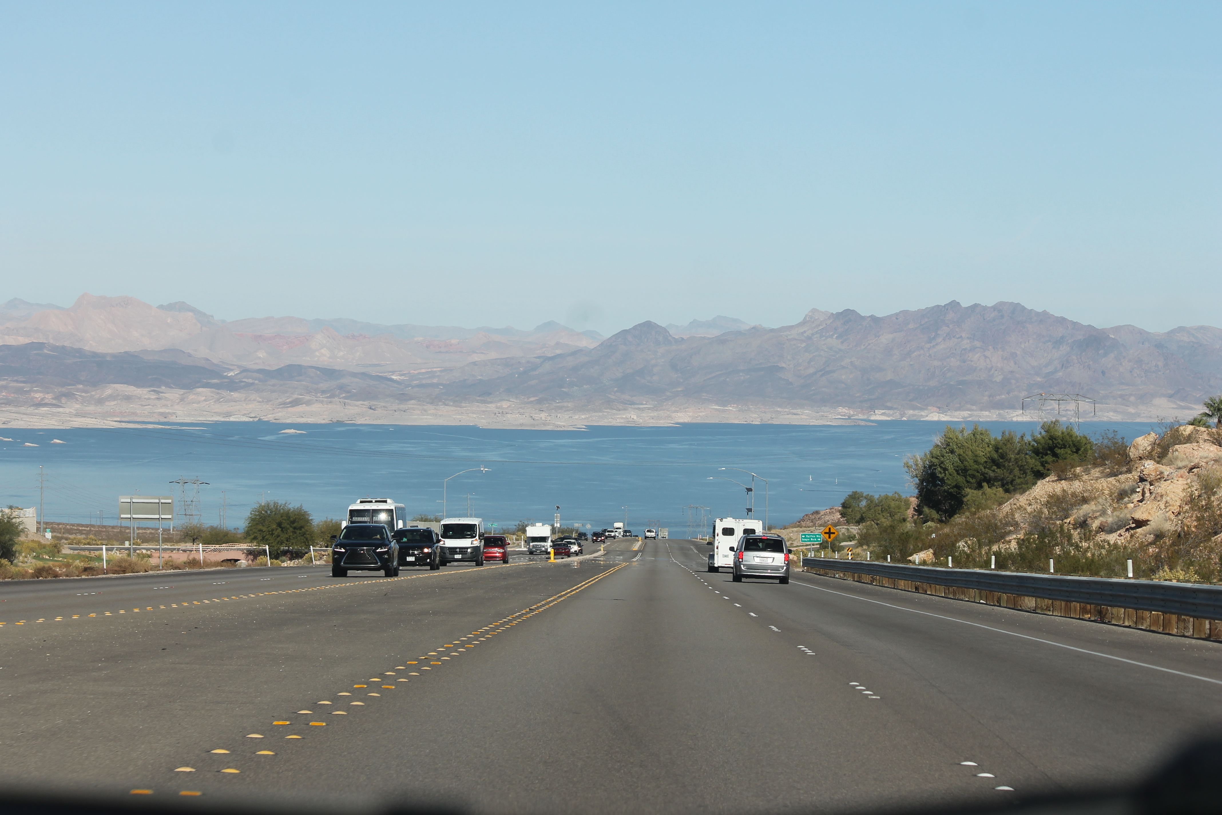 Traffic on a highway descending toward blue Lake Mead and desert mountains.