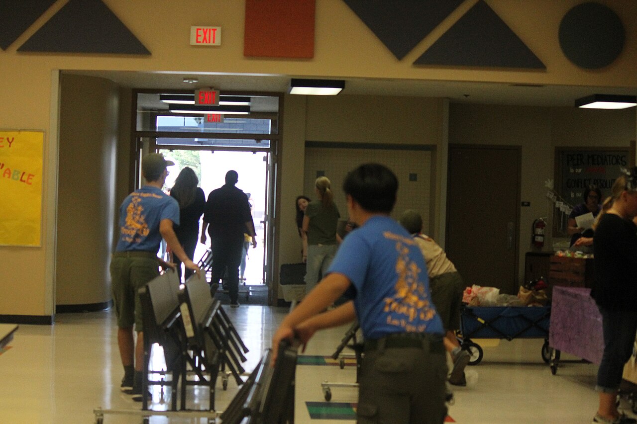 Youth volunteers moving folding chairs and tables inside a school.