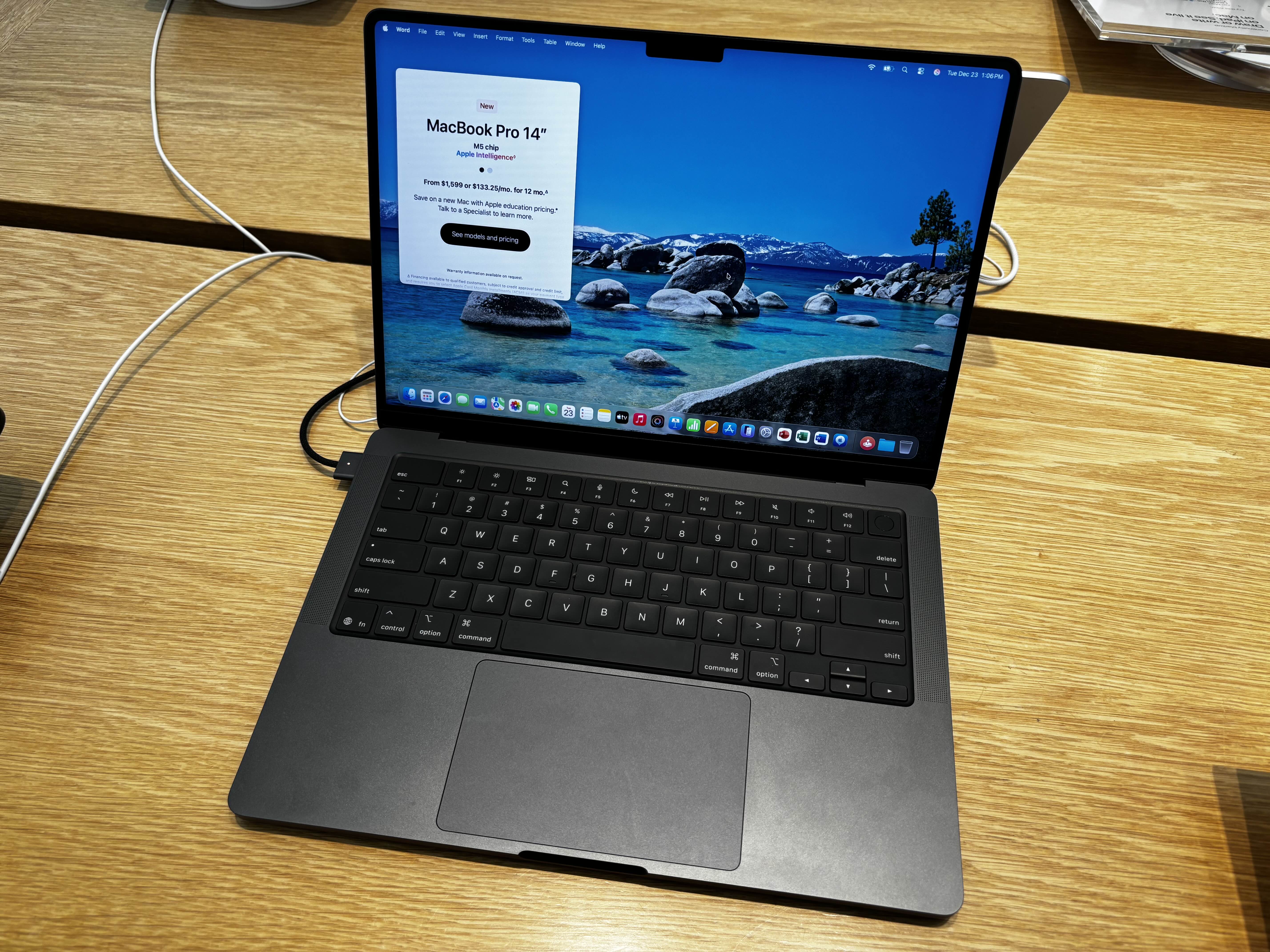 A black MacBook Pro on a wooden display table, showing its desktop and an archival store information card