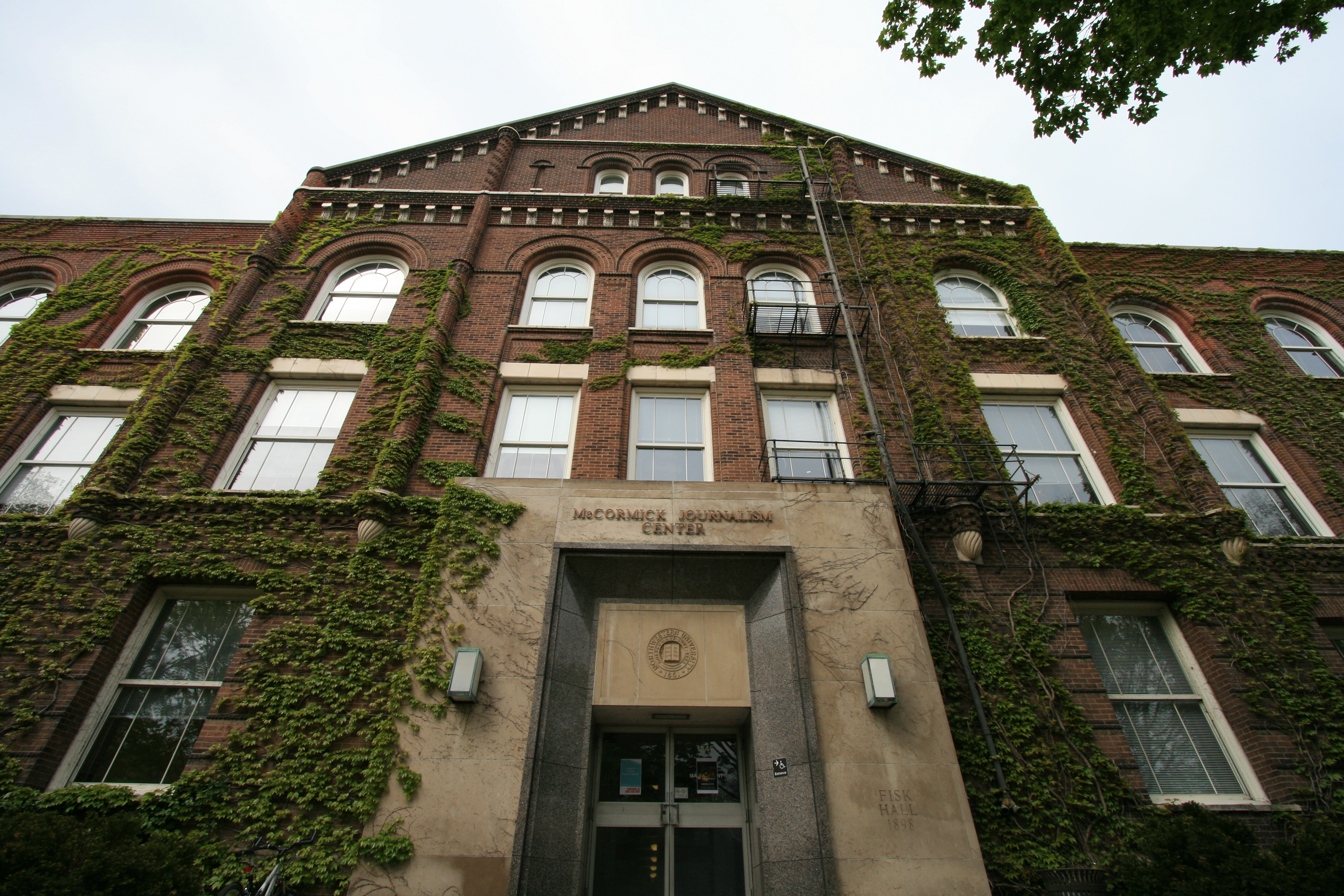Fisk Hall’s stone entrance and brick facade framed by trees.