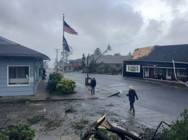 Storm debris beside a road and damaged buildings.