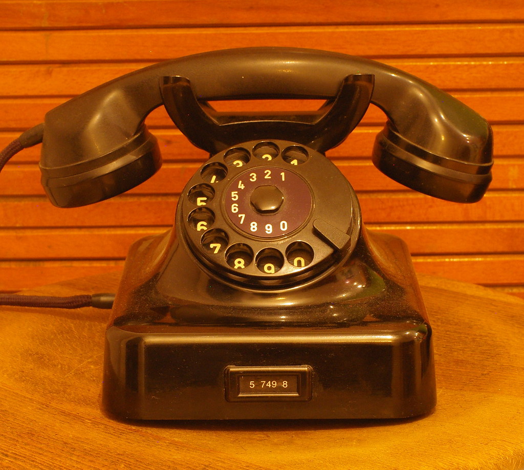 A black rotary telephone on a wooden surface.