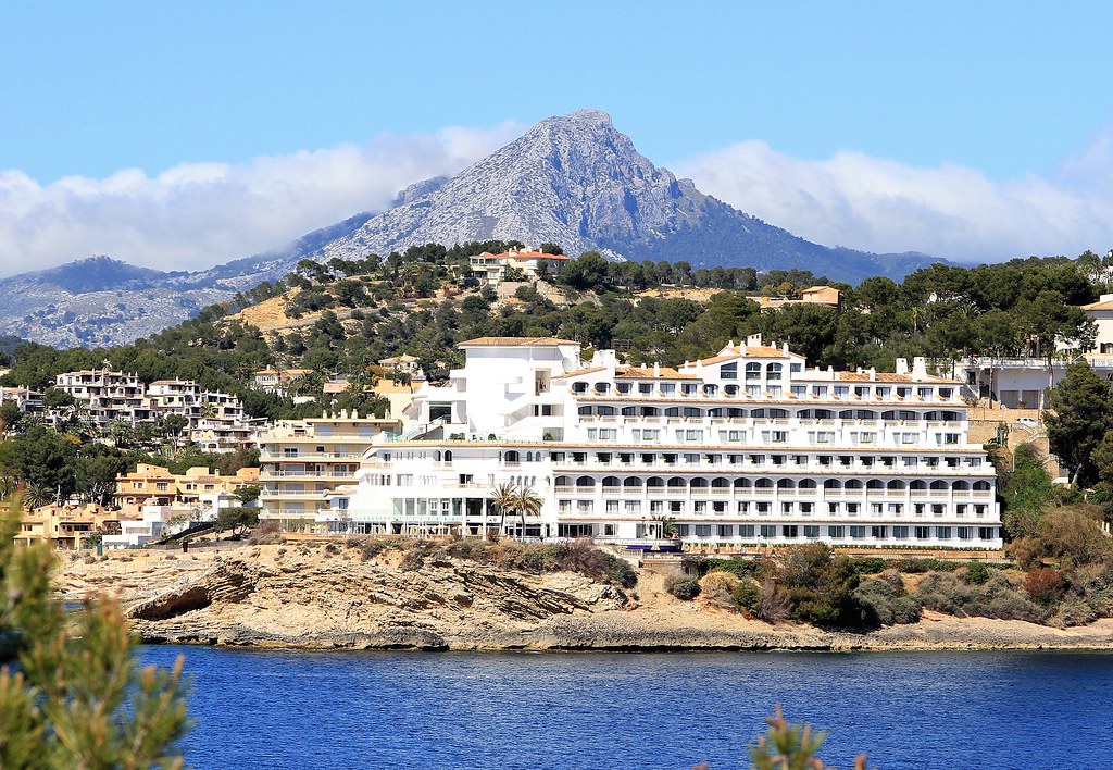 A seaside hotel stands below a rocky mountain.