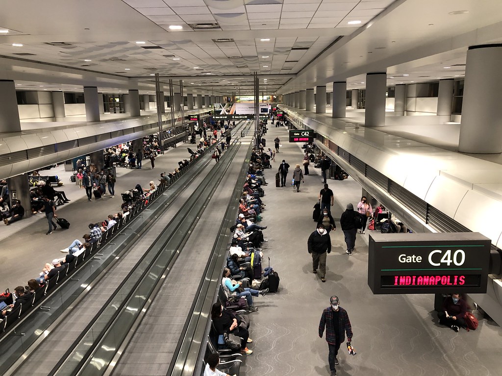 Passengers wait along airport concourse gates.