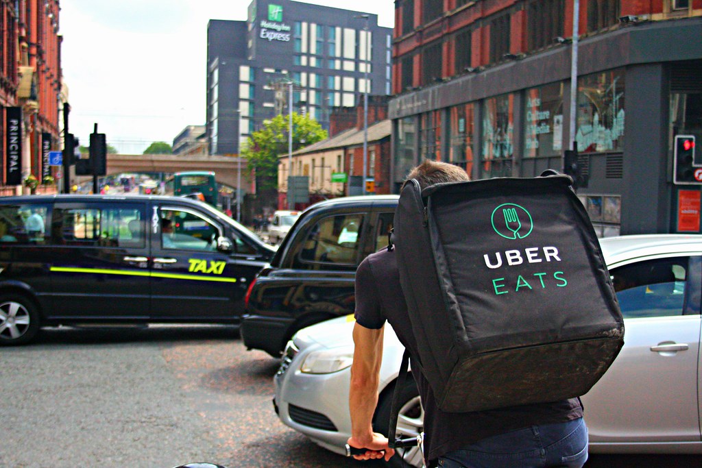 Delivery rider with a branded bag beside city traffic.