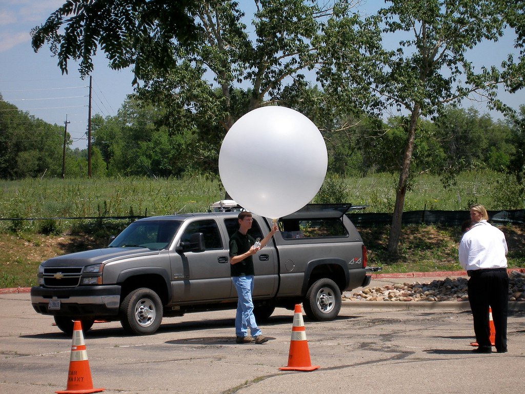 A person holds a weather balloon beside a pickup truck.