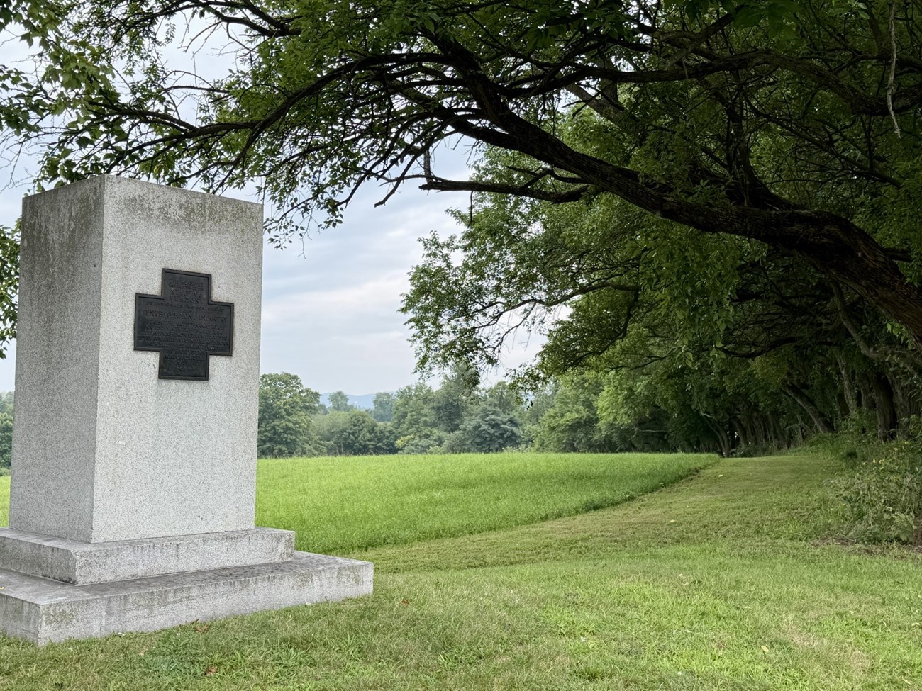 A stone monument stands beside a grassy trail.