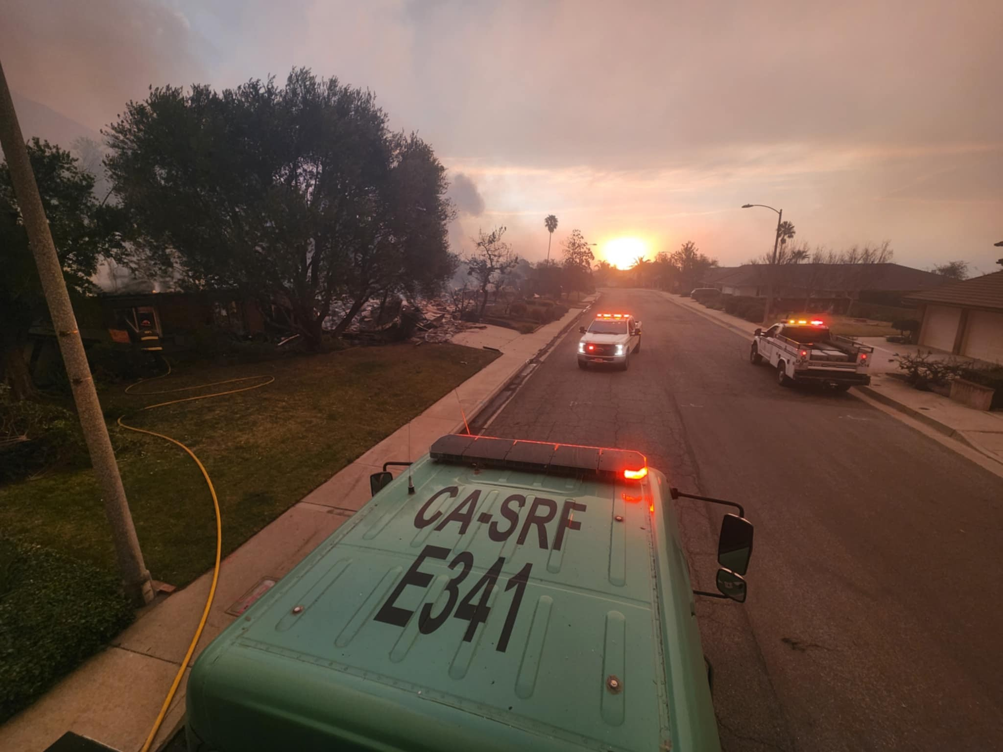 A Forest Service engine marked E341 and emergency vehicles on a smoke-filled residential street during the Eaton Fire.
