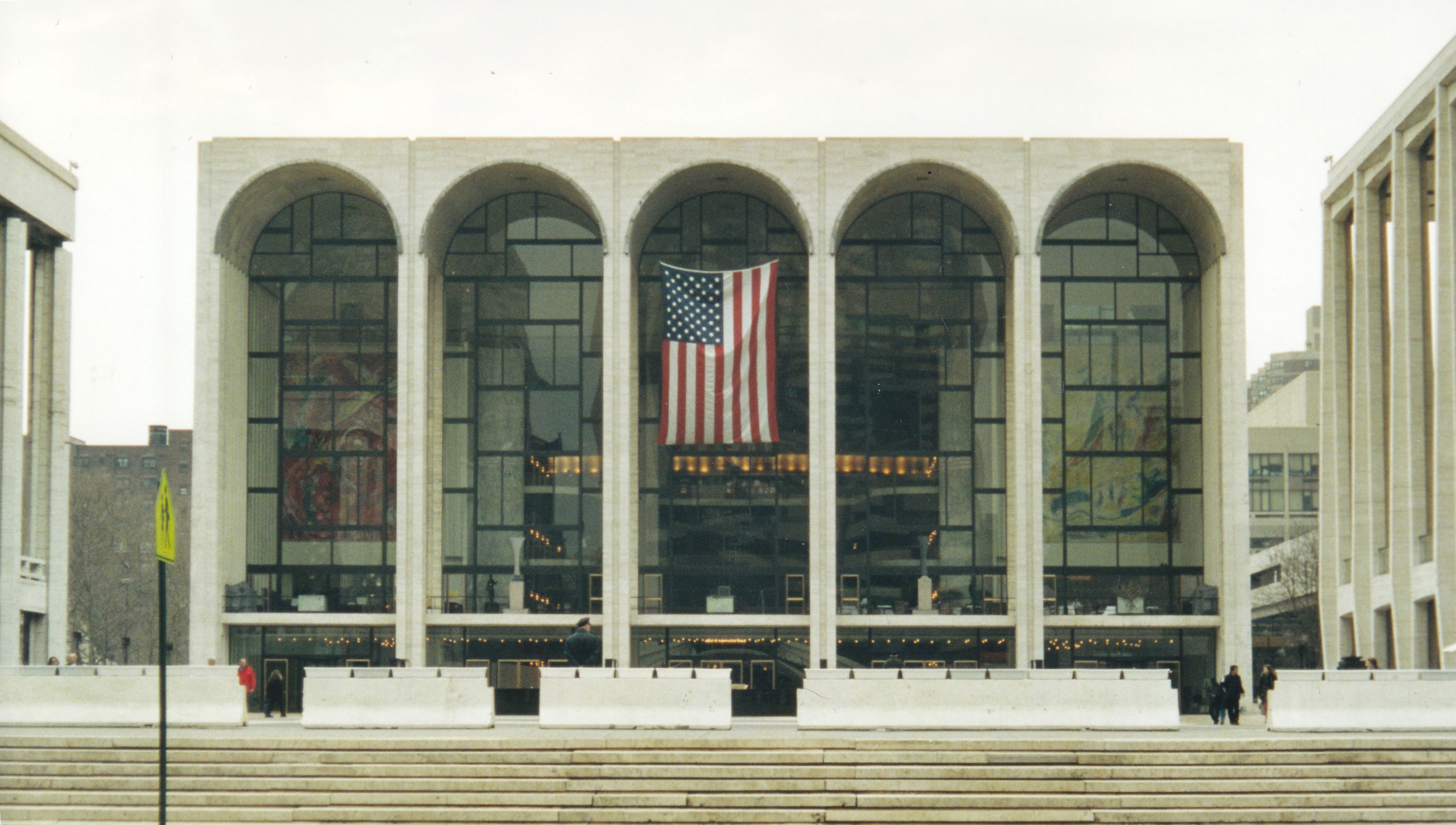 The Metropolitan Opera House’s arched facade with an American flag and plaza steps.