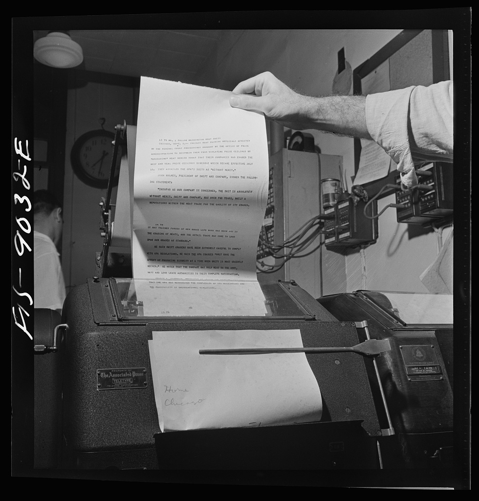 A hand lifts a paper dispatch from a teletypewriter.