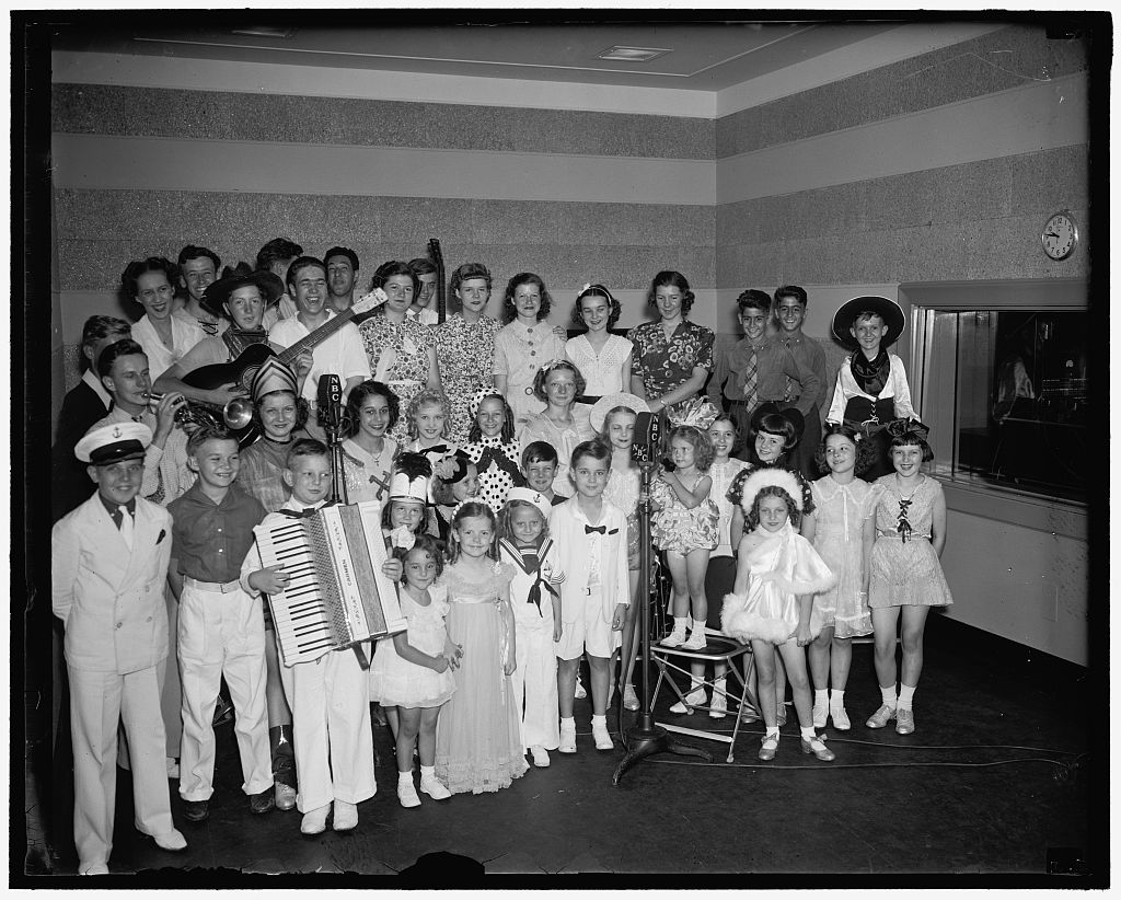 Children and adults gather around NBC microphones.