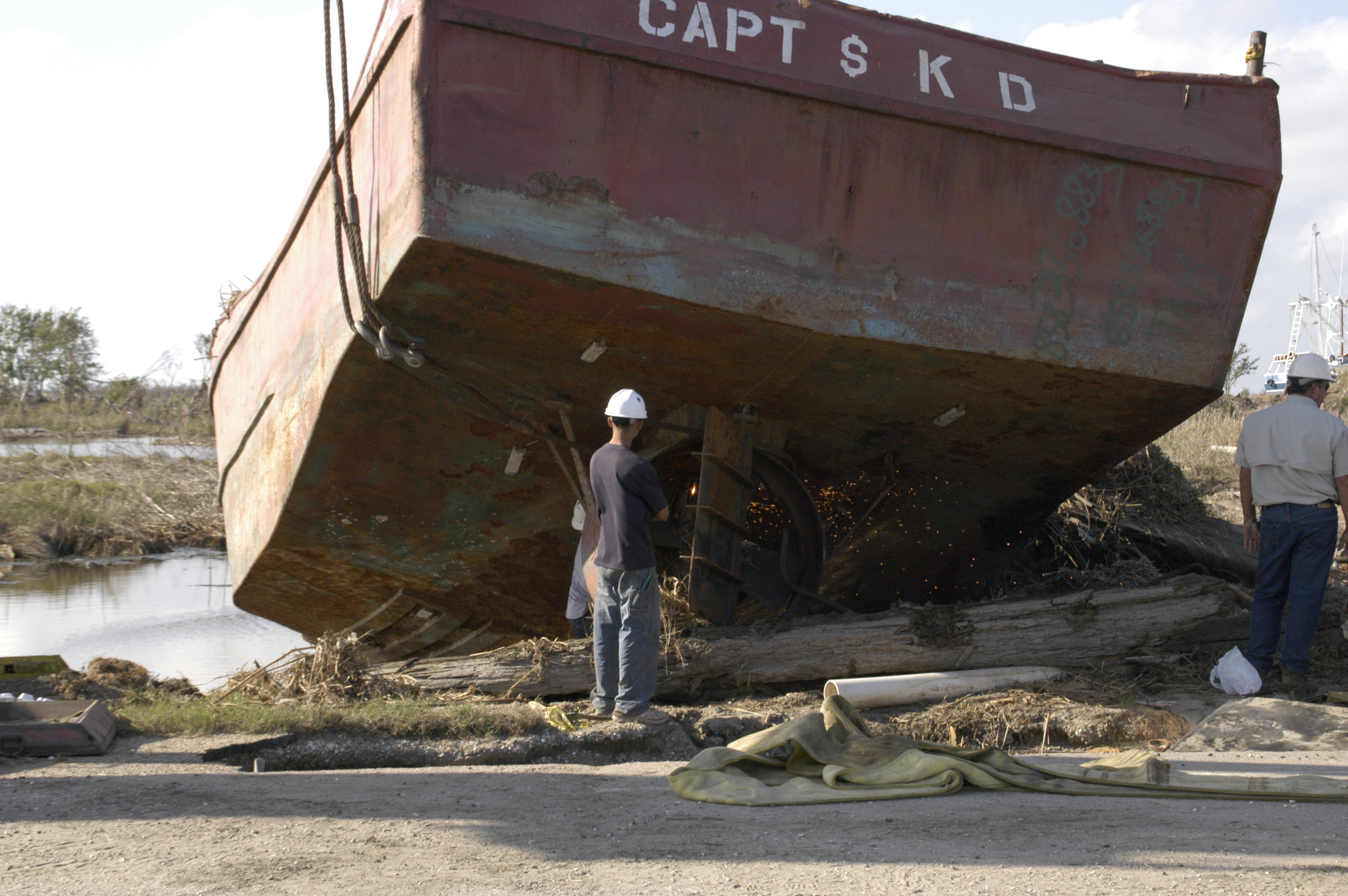Workers cut debris beneath a displaced boat.