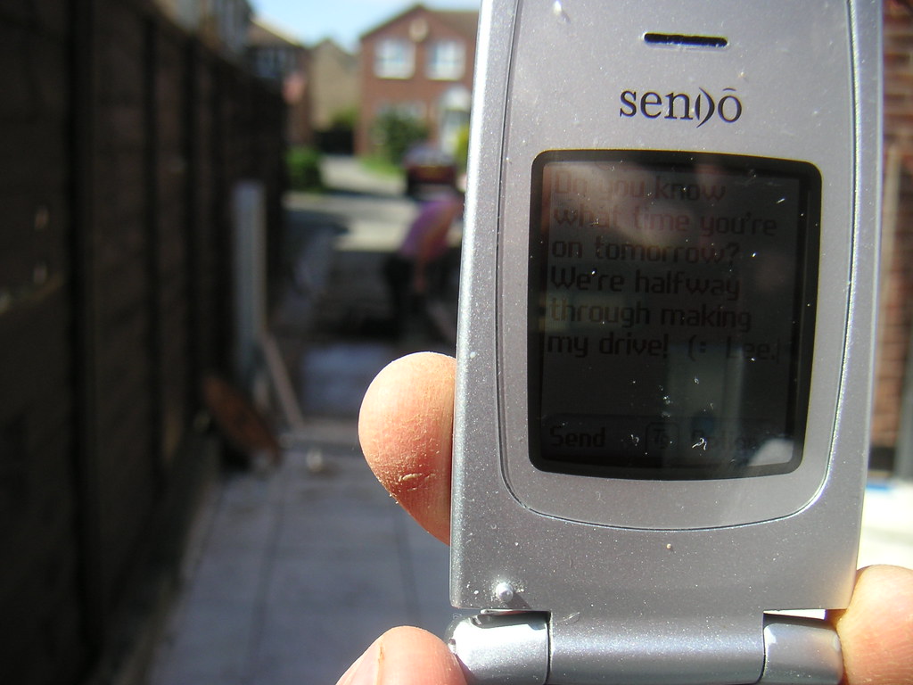A hand holds a flip phone displaying a text message.