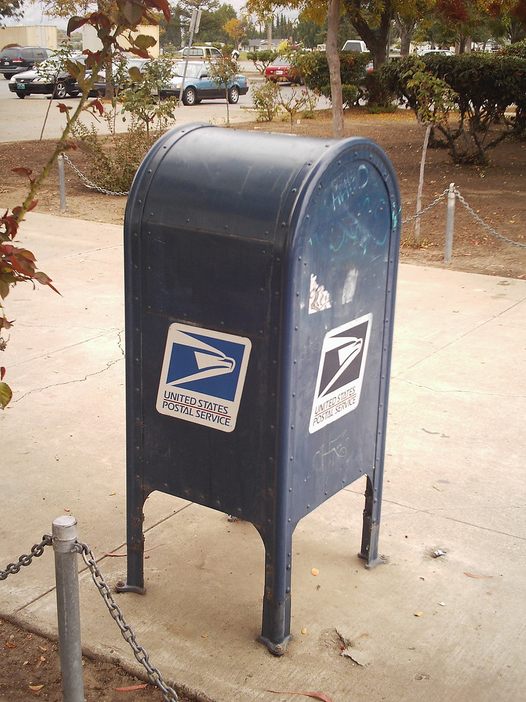 A blue USPS collection box stands beside a path.