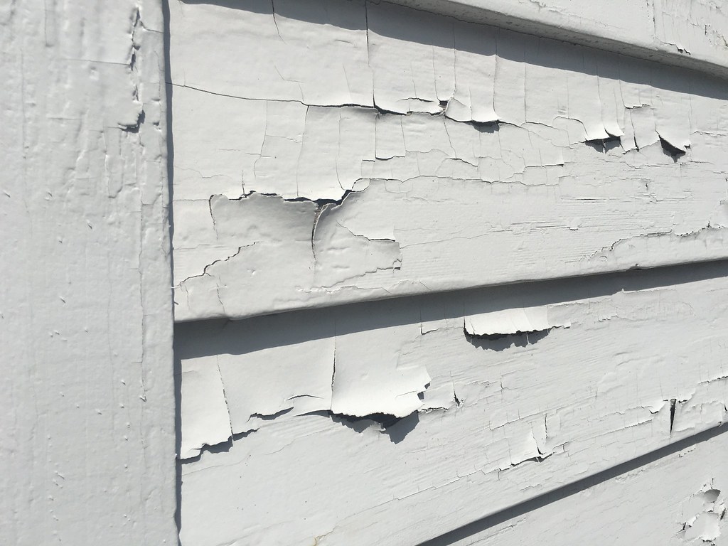 White paint flakes away from overlapping wooden boards.