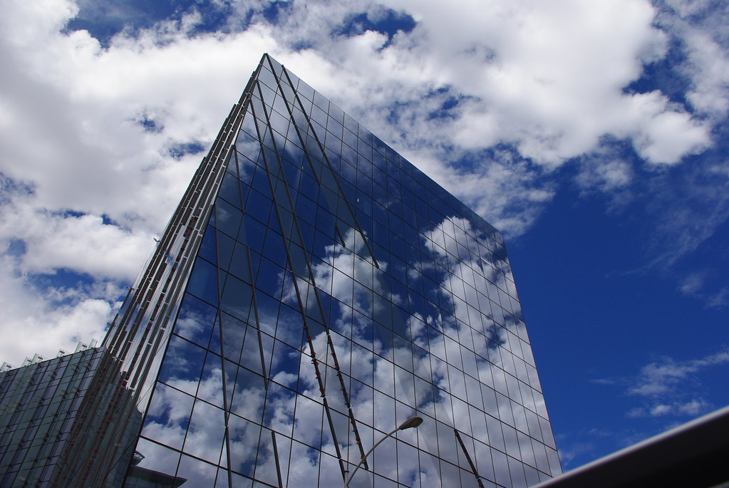 Glass City Hall exterior reflects clouds under a blue sky.