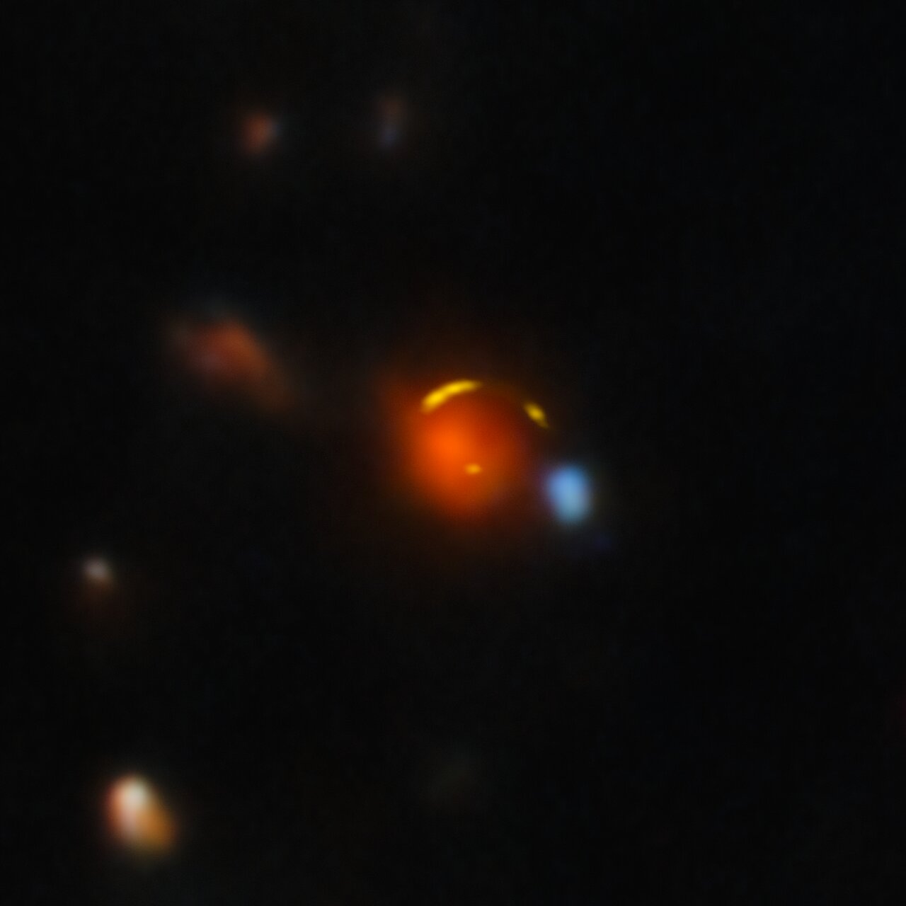 Yellow galaxy arcs around a red foreground galaxy.