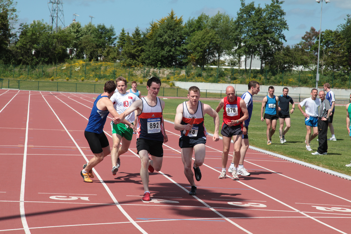 Runners pass a baton on a track.