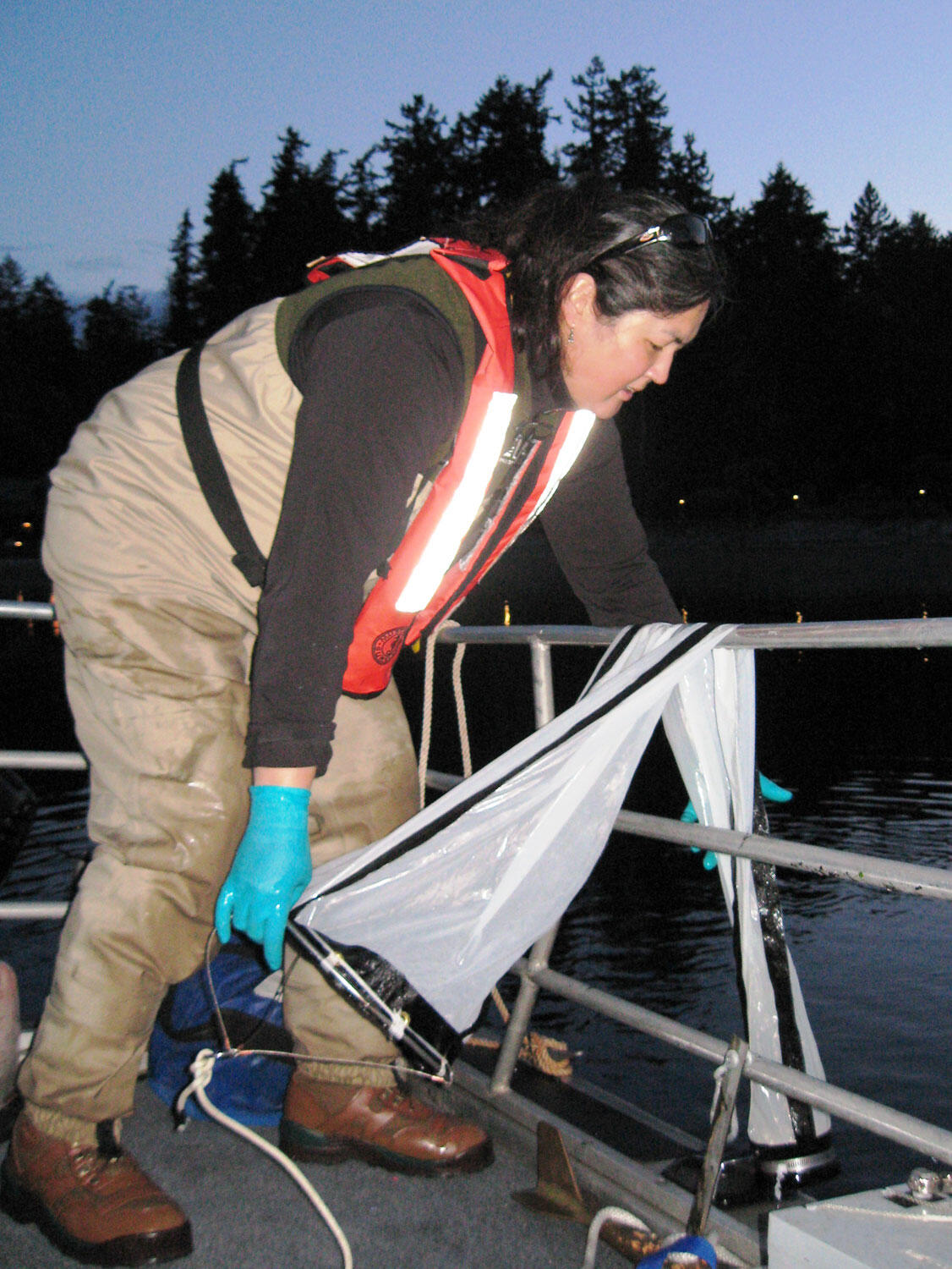 USGS crew member retrieves a small plankton net beside a boat railing.