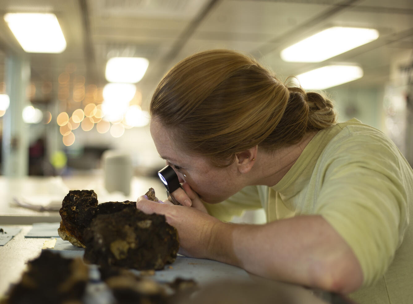 Research oceanographer examines a dark rock with a hand lens.