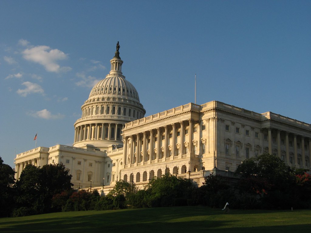 Capitol dome and stone facade above trees and lawn.