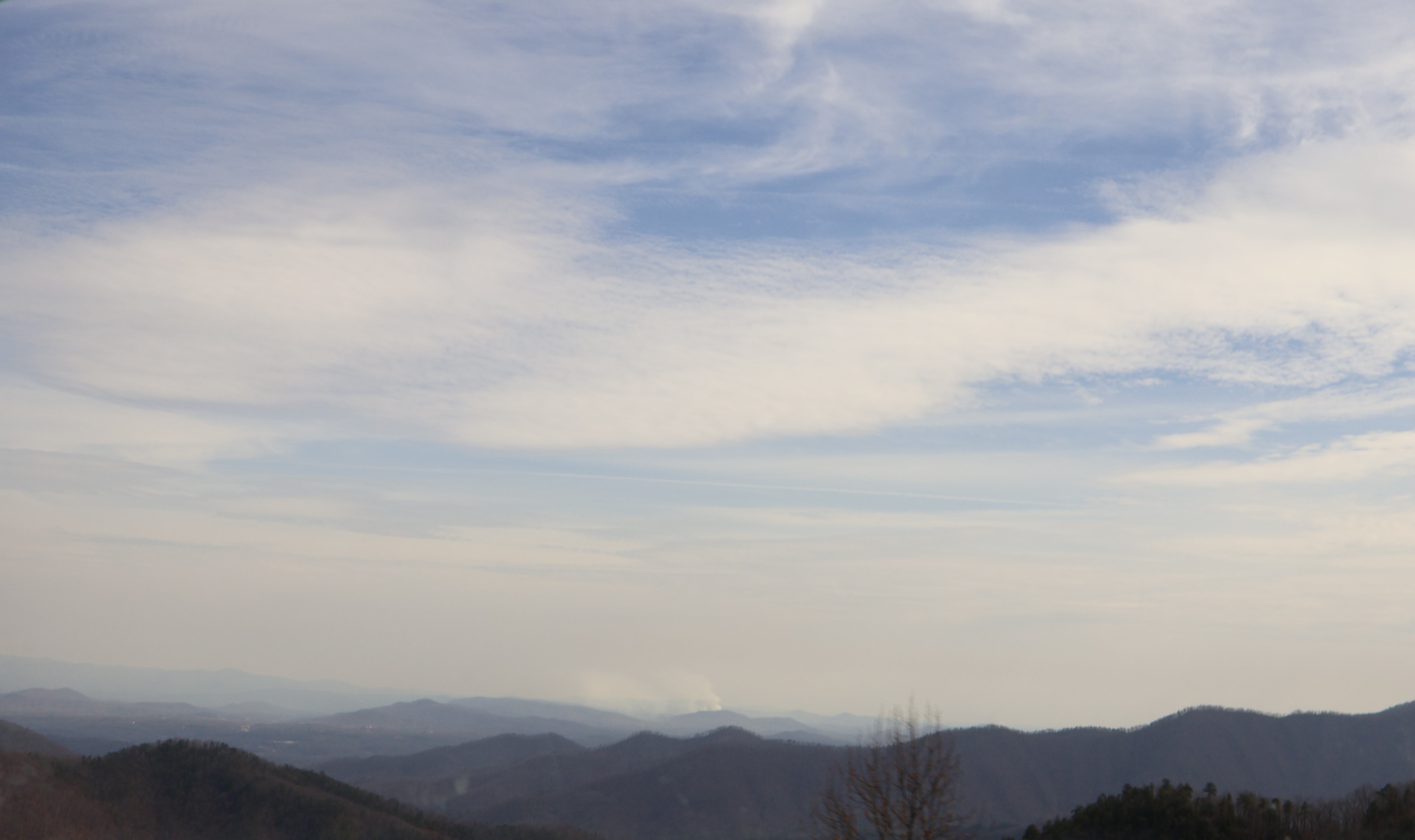 Layers of wooded mountain ridges beneath a pale, clouded sky, viewed from the Blue Ridge Parkway.