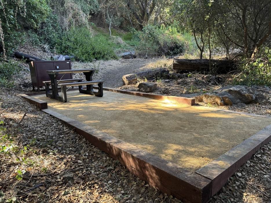A tent pad, picnic table and storage box among trees at Prisoners Harbor.