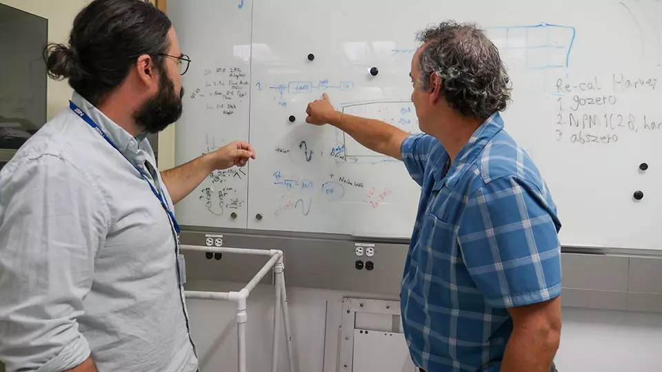 Two researchers discuss diagrams on a whiteboard.