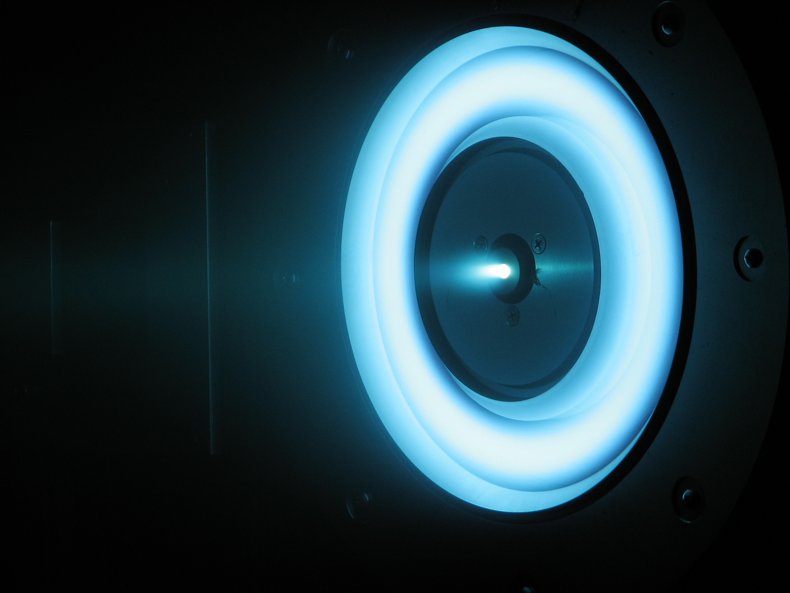 A xenon ion thruster glows blue in a chamber.