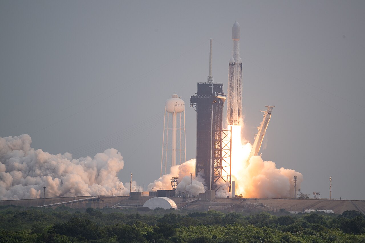 Falcon Heavy rocket lifting beside a launch tower.